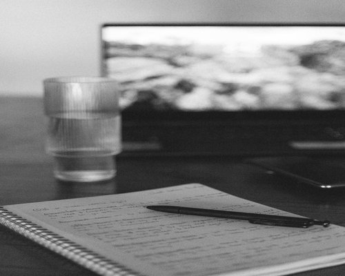 Organized workspace showing a notebook, water glass, and natural light coming from the side